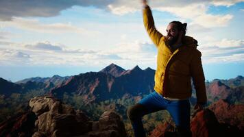 Proud explorer reaches the top of the mountain feeling satisfied and pleased with his accomplishment, scenic background of mountains and sky. Self improvement and new horizons. Camera A. video