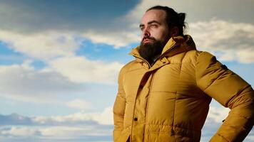 Nature lover stands at the edge of a breathtaking mountain range, looking at the scenic background of towering peaks and vast sky. Young man enjoying adventure and outdoor exploration. Camera B. video