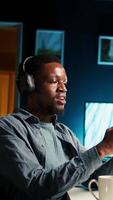 Vertical African american man waving and attending a web meeting from his urban apartment. Engaged male freelancer discussing work remotely with coworkers using wireless for conferencing call. Camera A. video
