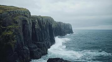 A rugged coastline with cliffs and waves crashing against the shore under a cloudy sky photo