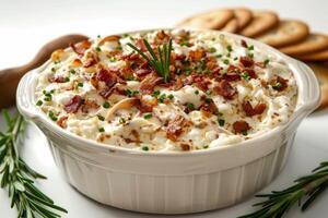 Creamy dish topped with bacon and herbs, served in a white bowl with snacks nearby. photo