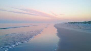 A serene beach at dawn with calm waves and soft pastel colors reflecting on the water photo