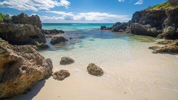 A serene beach scene with clear water, rocky formations, and a bright blue sky photo