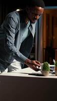 Vertical African American guy sitting at his home office and researching data, starting his day with a coffee cup planning tasks. Productivity through online resources to manage daily activities. Camera A. video