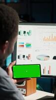 Vertical Young person does remote work using data finances with a green screen, examining statistics at his workstation. Investment advisor planning new strategy to obtain funds for development. Camera B. video