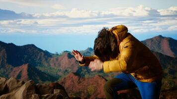 Battling intense wind and searching for better telephone signal, young hiker acting reckless distracted by smartphone on mountain top. Tumbling on the steep cliffs of a scenic peak. Camera B. video