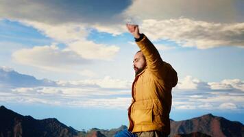 Traveler reaches new heights and doing a victory dance on mountain top, feeling the satisfaction and motivation. Breathtaking view of the mountain range and sky reflects adventure. Camera B. video