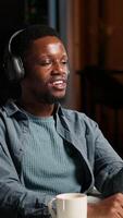 Vertical African american man waving and attending a web meeting from his urban apartment. Engaged male freelancer discussing work remotely with coworkers using wireless for conferencing call. Camera B. video