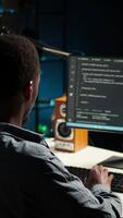 Vertical African american expert at desk using pc for programming and data analysis. Young networking expert working from his home setup, manages information technology and data center. Camera A. video