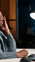 Vertical Black developer feeling exhausted and trying to meet task deadline, working hard to finish report in time and dealing with a headache. African american guy being under stress with pressure. Camera B. video