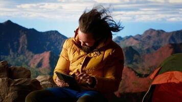 Traveler tries to stay connected in the wilderness but struggles with weak signals, dangerous wind at the top of the mountain. Hiker setting up his tent on a rocky windy peak. Camera B. video