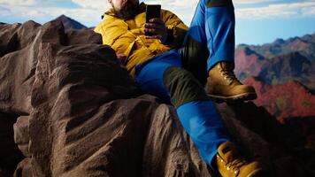 Traveler in warm clothing scrolling social media on top of the mountain peak, person always connected with a strong signal and obsessed with technology. Climbing the hills. Camera A. video