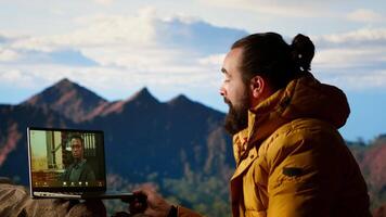 Workaholic explorer meeting with colleagues on online call, enjoying a strong signal high speed internet on top of the mountain. Young hiker CEO with dependency. Camera B. video