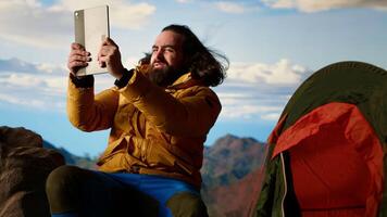 Reckless explorer struggling with wind and weak signal keep internet connection, camping on a scenic rocky mountain peak. Hiker in danger with extreme cold weather, foolish. Camera B. video