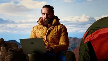 Workaholic explorer always connected and addicted to uninterrupted work, opening his laptop on the mountain top. Young hiker with internet dependency enjoys strong signal. Camera B. video