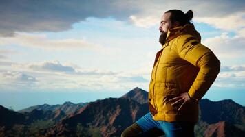Nature lover stands at the edge of a breathtaking mountain range, looking at the scenic background of towering peaks and vast sky. Young man enjoying adventure and outdoor exploration. Camera A. video