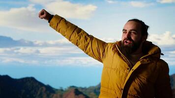 Adventure seeker stands on top a high altitude mountain for a breathtaking view, pleased hiker raising his arms and screaming in satisfaction. Conquering fears and challenges. Camera B. video