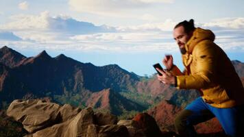 Reckless trekker risking his life focusing on his phone and falling, overwhelmed by bad weather and weak signal loses balance on a treacherous mountain peak. Foolish hiker. Camera B. video