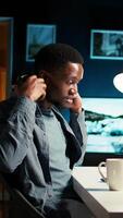 Vertical African American guy waving at a call connection with workmates, working remotely from his apartment and participating in executive meetings. Virtual communication. Camera A. video