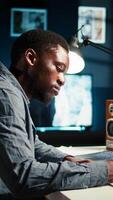 Vertical Self employed Black man multitasking at home taking handwritten notes and browsing the web for project research. Managing schedule and tasks with a planner to boost productivity. Camera A. video