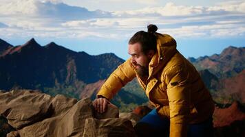 Proud explorer celebrates on top of a high altitude mountain peak, surrounded by rugged hills and dramatic clouds. Triumphant pose captures the thrill of climbing to success. Camera B. video
