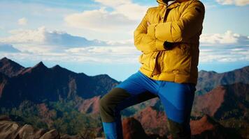 Hiker stands victorious on a mountain peak with arms raised in triumph, celebrating his personal achievement with a successful climb. Scenic view and endless sky for freedom. Camera A. video