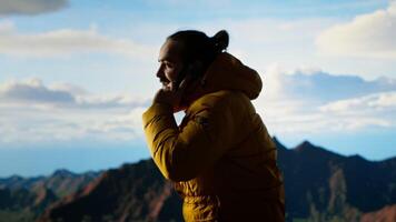 Trekker enjoys the high altitude landscape and making a phone call, panoramic mountain views and crisp air provide the perfect scene for relaxation. Using strong signal on his smartphone. Camera B. video