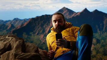 Traveler in warm clothing scrolling social media on top of the mountain peak, person always connected with a strong signal and obsessed with technology. Climbing the hills. Camera B. video