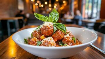 Meatballs in tomato sauce, garnished with basil and parmesan cheese, served in a white bowl on a wooden table in a restaurant. photo