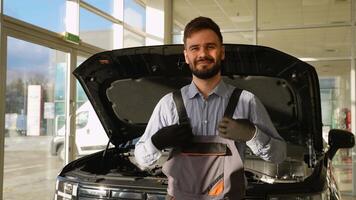 Smiling auto mechanic standing in front of open car hood video