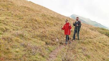 Hikers woman and man walking on narrow path in mountain with sticks in hands. video