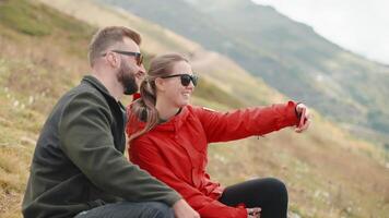 happy hikers taking selfie by smartphone on slope of mount during halt, joyful smiling travellers video