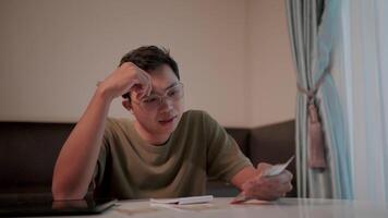 Young man intently counting cash. A young man with glasses is intently calculating document expenses at his desk, showing his dedication and commitment to his work. video