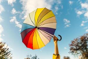 young woman standing with a multi-colored umbrella and rotates it against with a blue sky, photo