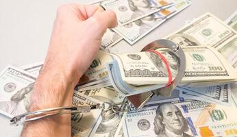 Folded hands and handcuffed hands resting on a table in front of money. photo