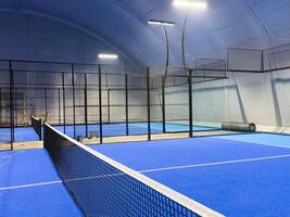 blue court for padel with construction created by mesh and the glass back walls. photo