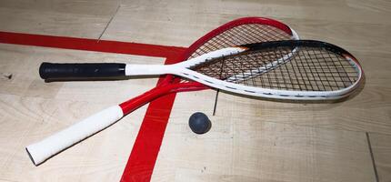 Two rackets and two squash balls lie on the parquet floor. Horizontal photo