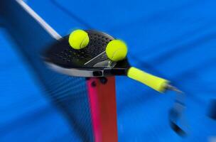 A padel or paddle tennis racket and a bright yellow tennis ball lie on a blue court. photo