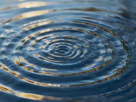 A close-up macro shot of gentle water ripples forming circular light reflections. photo