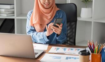 Muslim woman in hijab using smartphone while working at a desk with financial documents. photo