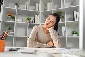 Stressed office worker experiencing neck pain while sitting at a desk with paperwork and a computer. photo