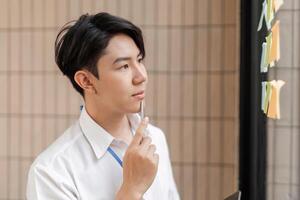 Young professional contemplating sticky notes on glass wall, strategizing tasks and improving workflow in modern office. photo