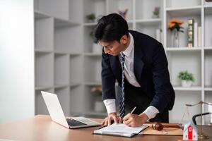 Young businessman writing notes and reviewing documents while standing in a modern office environment. photo