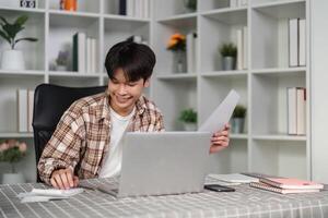 Smiling young man analyzing financial documents and using a laptop for planning. photo