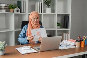 Muslim woman in hijab presenting a report with a pie chart during a call in a modern office. photo