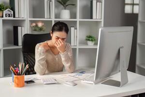 Stressed office worker rubbing her forehead in frustration while working on a computer. photo