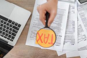 Close-up of hands using a magnifying glass on tax documents, emphasizing important financial information. photo