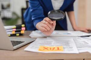 Close-up of an accountant using a magnifying glass on tax documents in a professional setting. photo