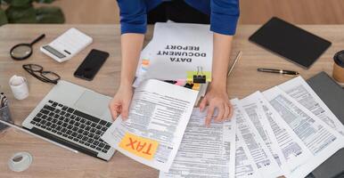 Accountant sorting tax paperwork and using a laptop in a contemporary office setting. photo