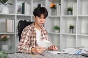 Young man managing finances at home, reviewing bills and using a calculator in a modern workspace. photo